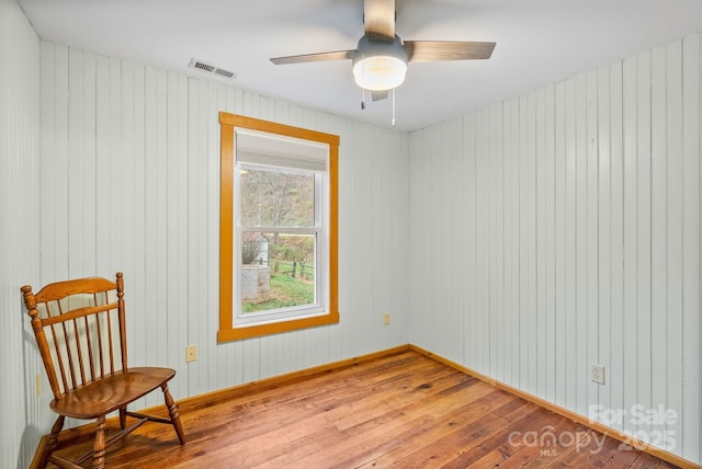 living area with hardwood / wood-style floors, ceiling fan, and wooden walls