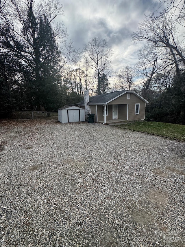 bungalow-style home with covered porch, a chimney, a storage unit, and an outbuilding