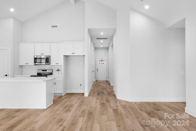 kitchen with high vaulted ceiling, decorative backsplash, appliances with stainless steel finishes, light hardwood / wood-style floors, and white cabinetry