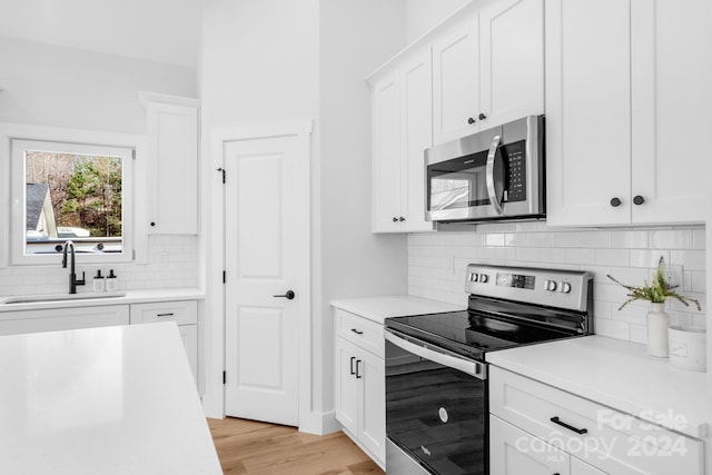 kitchen featuring white cabinetry, sink, tasteful backsplash, appliances with stainless steel finishes, and light wood-type flooring