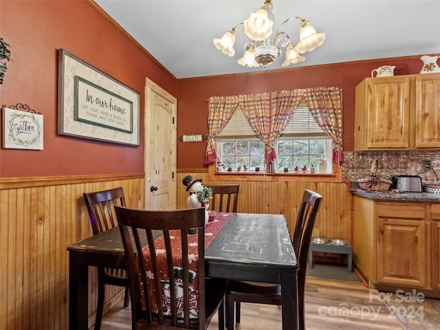 dining space featuring light wood-type flooring, an inviting chandelier, and wooden walls