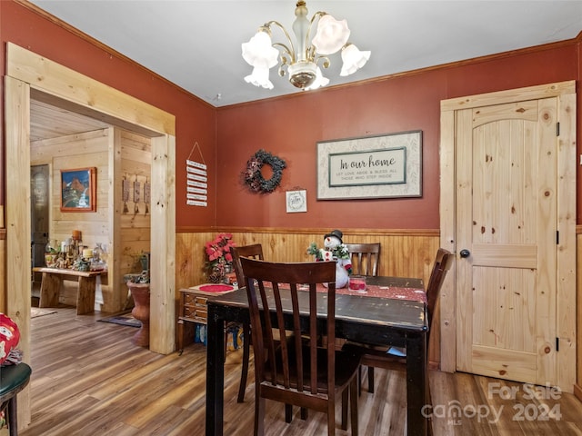 dining area with wood walls, wood-type flooring, and an inviting chandelier