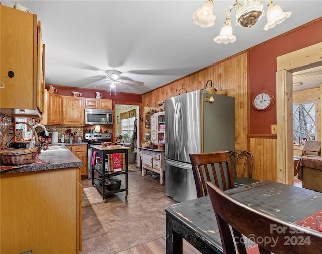 kitchen with sink, stainless steel appliances, hanging light fixtures, and wood walls