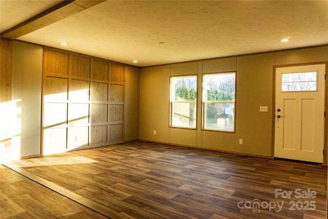 entryway with a textured ceiling, dark wood-type flooring, and wooden walls