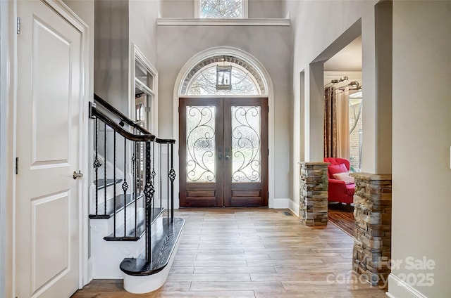 foyer entrance featuring a towering ceiling, light hardwood / wood-style floors, and french doors