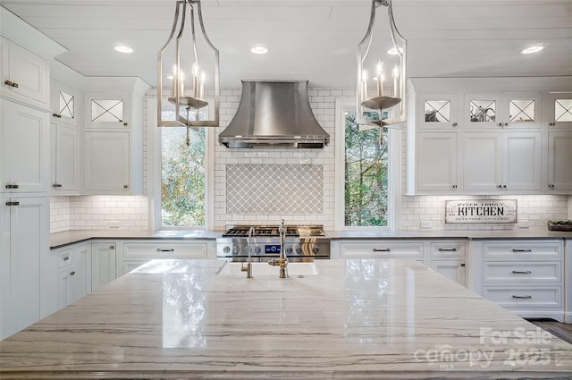 kitchen with hanging light fixtures, wall chimney range hood, and white cabinets