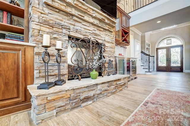 foyer entrance featuring french doors, crown molding, light hardwood / wood-style floors, and a high ceiling