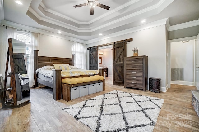 bedroom with crown molding, light hardwood / wood-style flooring, ceiling fan, a raised ceiling, and a barn door