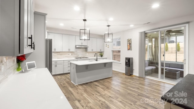 kitchen with a kitchen island with sink, sink, hanging light fixtures, light hardwood / wood-style flooring, and stainless steel refrigerator