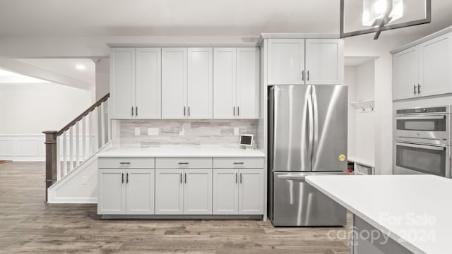 kitchen with white cabinets, appliances with stainless steel finishes, backsplash, and light hardwood / wood-style floors