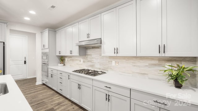 kitchen with white cabinets, dark hardwood / wood-style floors, appliances with stainless steel finishes, and tasteful backsplash