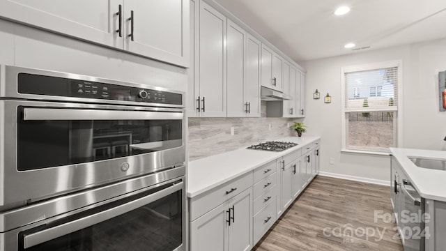 kitchen featuring sink, backsplash, light hardwood / wood-style floors, white cabinets, and appliances with stainless steel finishes