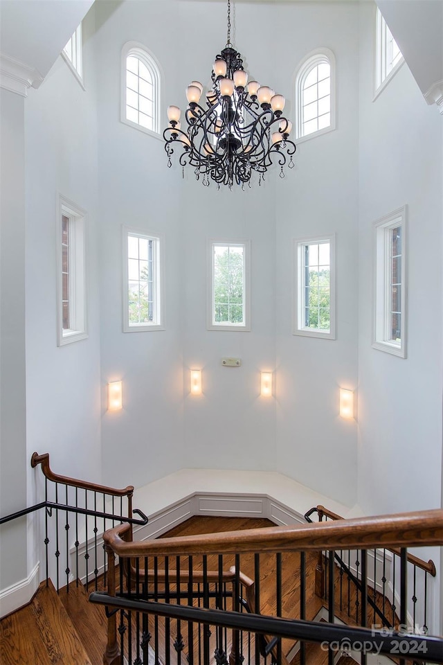 stairs featuring plenty of natural light, wood-type flooring, a high ceiling, and a notable chandelier