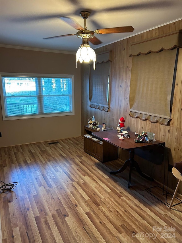 interior space featuring light wood-type flooring, ceiling fan, ornamental molding, and wood walls