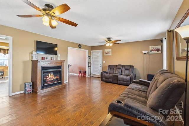 living room featuring ceiling fan, wood finished floors, a glass covered fireplace, and baseboards