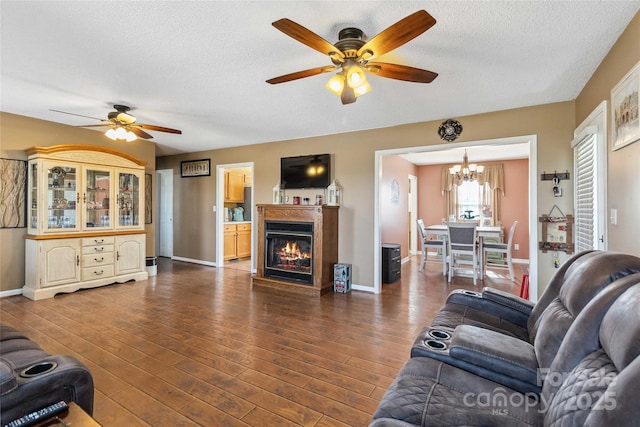 living area featuring a ceiling fan, a textured ceiling, dark wood finished floors, a glass covered fireplace, and a chandelier