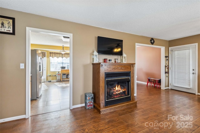 living room with a textured ceiling, wood finished floors, a glass covered fireplace, and baseboards