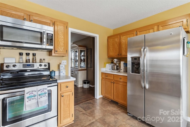 kitchen featuring stainless steel appliances, light countertops, a textured ceiling, baseboards, and dark tile patterned flooring