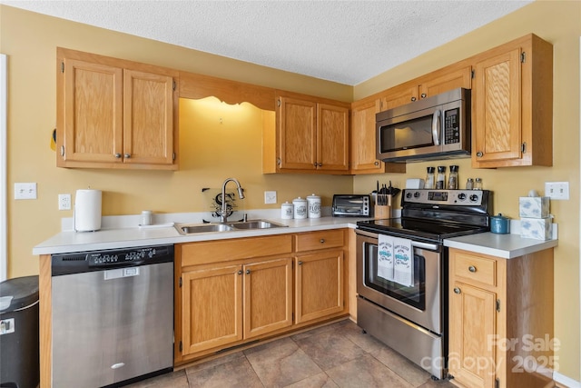kitchen with stainless steel appliances, a sink, light countertops, and a textured ceiling