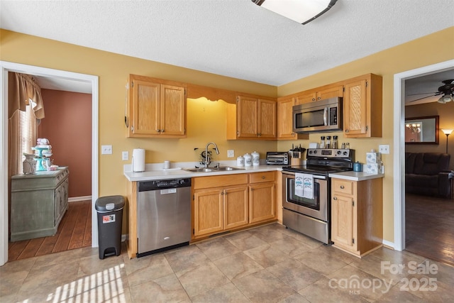 kitchen featuring appliances with stainless steel finishes, a sink, light countertops, a textured ceiling, and ceiling fan