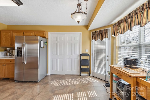 kitchen featuring stainless steel fridge with ice dispenser, light tile patterned floors, light countertops, brown cabinets, and a textured ceiling