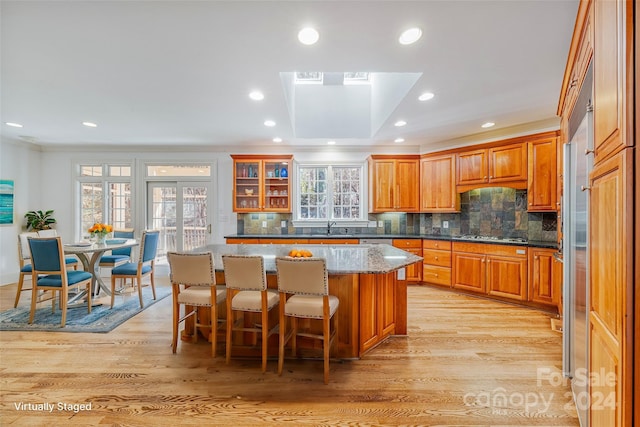 kitchen with light wood-type flooring, a center island, a wealth of natural light, and dark stone counters