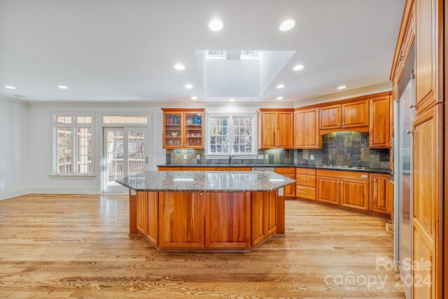 kitchen featuring dark stone counters, sink, decorative backsplash, light wood-type flooring, and a kitchen island