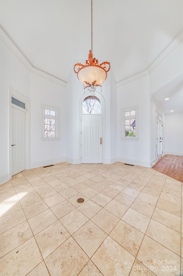 tiled entrance foyer featuring crown molding, lofted ceiling, and a notable chandelier