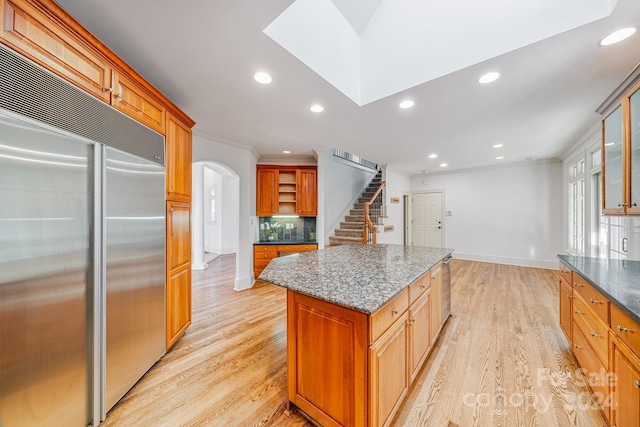 kitchen with dark stone counters, light wood-type flooring, stainless steel built in fridge, a kitchen island, and ornamental molding