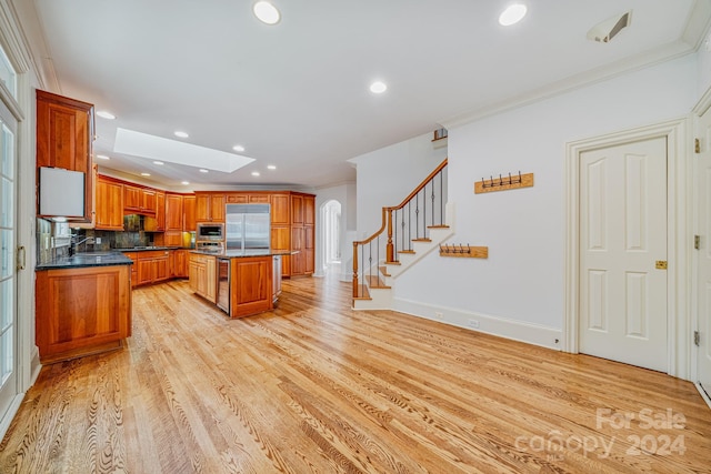 kitchen with a skylight, light hardwood / wood-style floors, ornamental molding, appliances with stainless steel finishes, and a kitchen island