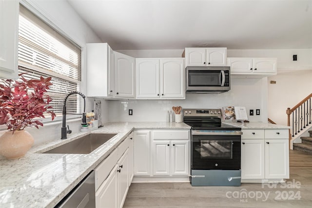 kitchen featuring appliances with stainless steel finishes, light stone counters, sink, light hardwood / wood-style floors, and white cabinetry