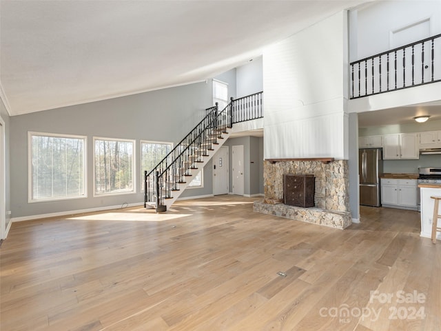 unfurnished living room featuring light wood-type flooring, high vaulted ceiling, and a stone fireplace