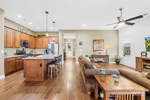 kitchen with appliances with stainless steel finishes, a breakfast bar, an island with sink, hardwood / wood-style flooring, and light stone countertops