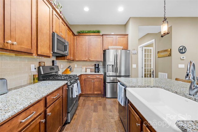 kitchen with sink, stainless steel appliances, tasteful backsplash, wood-type flooring, and decorative light fixtures