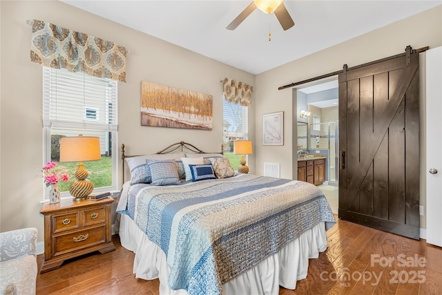 bedroom featuring hardwood / wood-style flooring, ceiling fan, a barn door, and ensuite bath