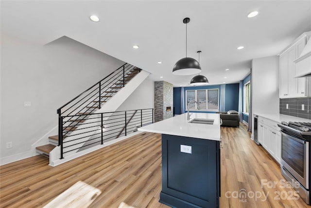 kitchen featuring decorative light fixtures, white cabinetry, sink, a kitchen island with sink, and stainless steel range oven