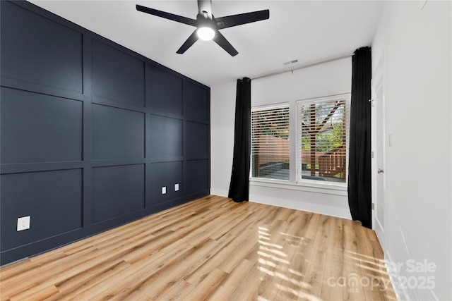 empty room with light wood-type flooring, visible vents, a decorative wall, and ceiling fan