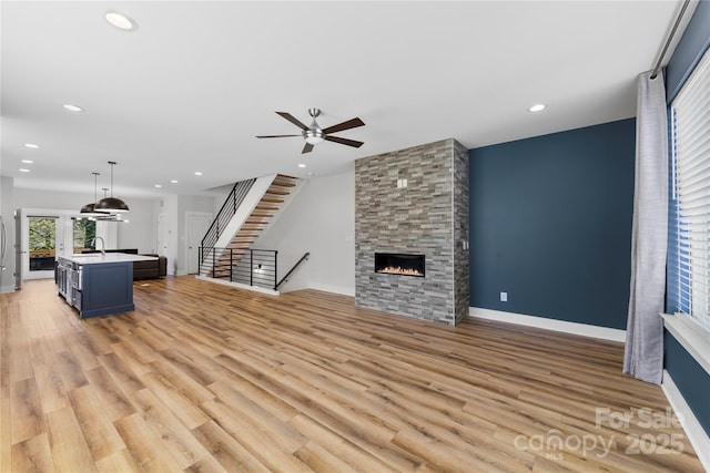 unfurnished living room featuring light wood finished floors, baseboards, stairway, a fireplace, and recessed lighting