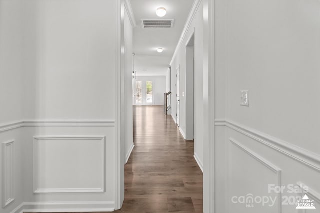 hall with dark wood-style flooring, wainscoting, visible vents, and a decorative wall