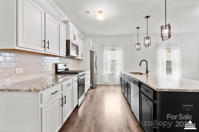 kitchen with tasteful backsplash, a center island with sink, appliances with stainless steel finishes, white cabinetry, and a sink