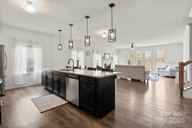 kitchen featuring dark wood-style floors, appliances with stainless steel finishes, dark cabinets, a kitchen island with sink, and a sink