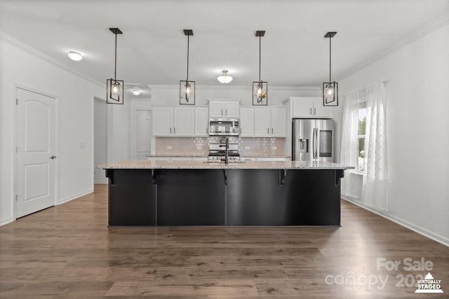 kitchen featuring stainless steel appliances, a sink, white cabinetry, backsplash, and a large island with sink