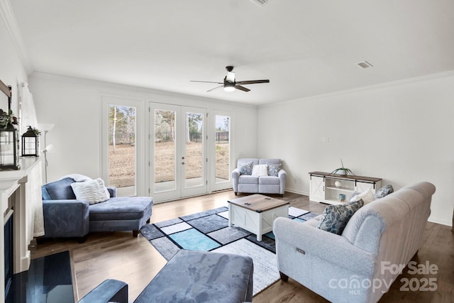 living room featuring crown molding, a fireplace, visible vents, a ceiling fan, and wood finished floors