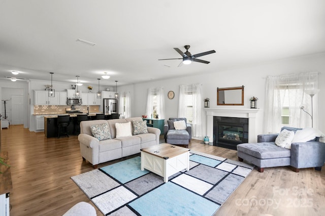 living room featuring a ceiling fan, a glass covered fireplace, and wood finished floors