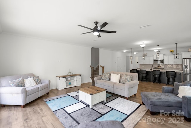 living room with ornamental molding, wood finished floors, ceiling fan, and stairs