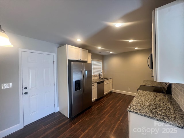 kitchen with stainless steel appliances, dark wood-type flooring, white cabinetry, a sink, and dark stone countertops