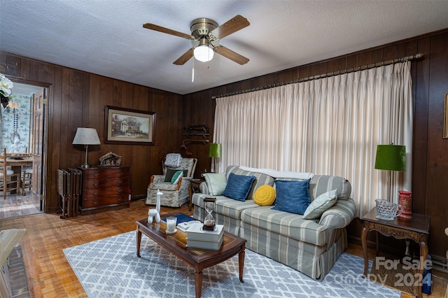 living room with wood-type flooring, a textured ceiling, ceiling fan, and wood walls