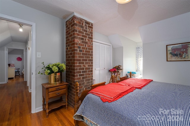 bedroom featuring hardwood / wood-style floors, vaulted ceiling, a textured ceiling, and a closet