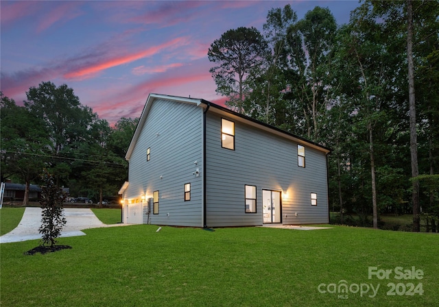 back house at dusk featuring a garage and a yard