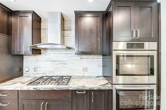 kitchen featuring decorative backsplash, appliances with stainless steel finishes, light stone countertops, wall chimney exhaust hood, and dark brown cabinets